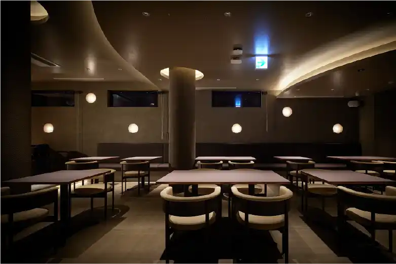曲線的な天井照明と円卓が並ぶ落ち着いた店内空間